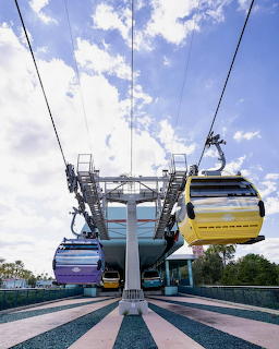 Multi-colored gondola cabins suspended on cables with blue sky and patterned pavement below
