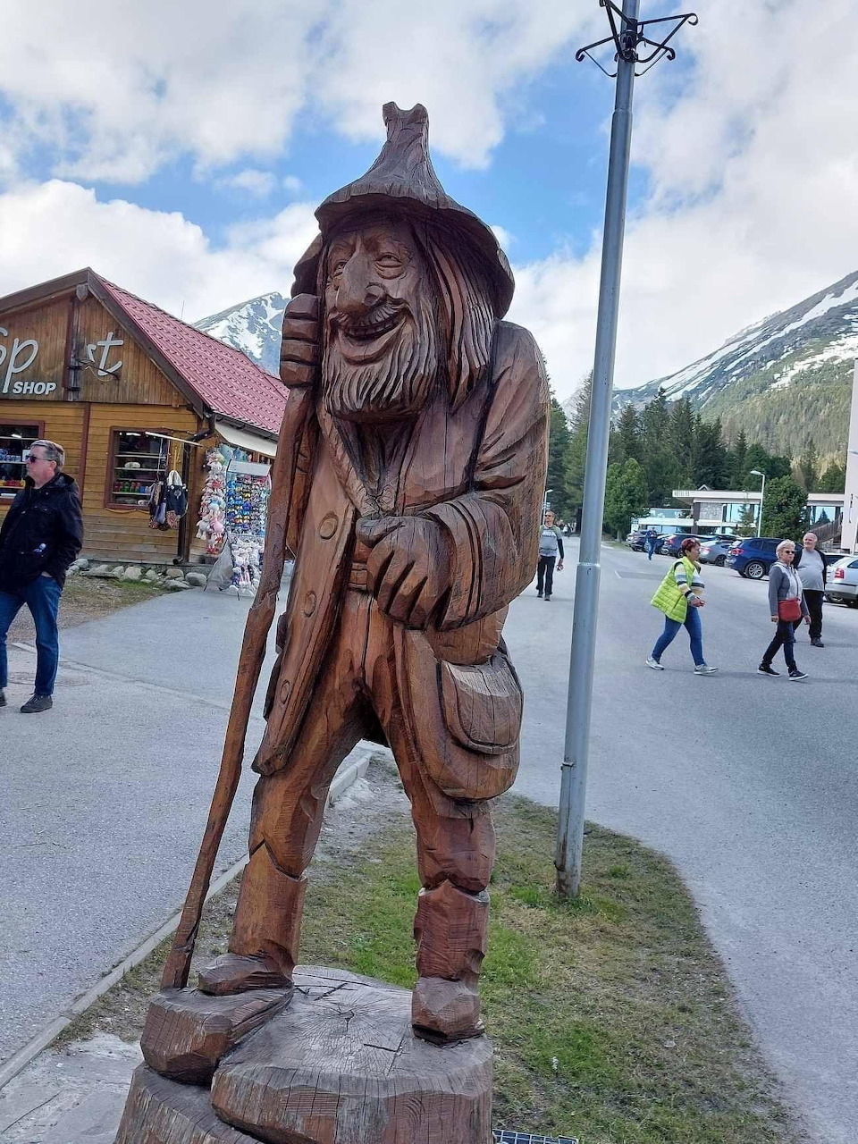 Carved wooden statue of bearded traveler with walking stick and hat in mountain village