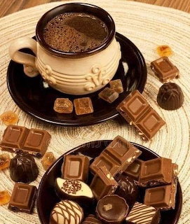 Cup of coffee on a dark saucer with chocolate bars, pralines, and caramel candies on a woven mat