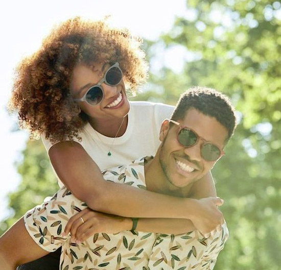 Smiling couple with sunglasses, woman on man's back outdoors in sunshine