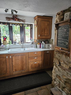 Rustic kitchen with wooden cabinets, stone wall, sink under window with garden view
