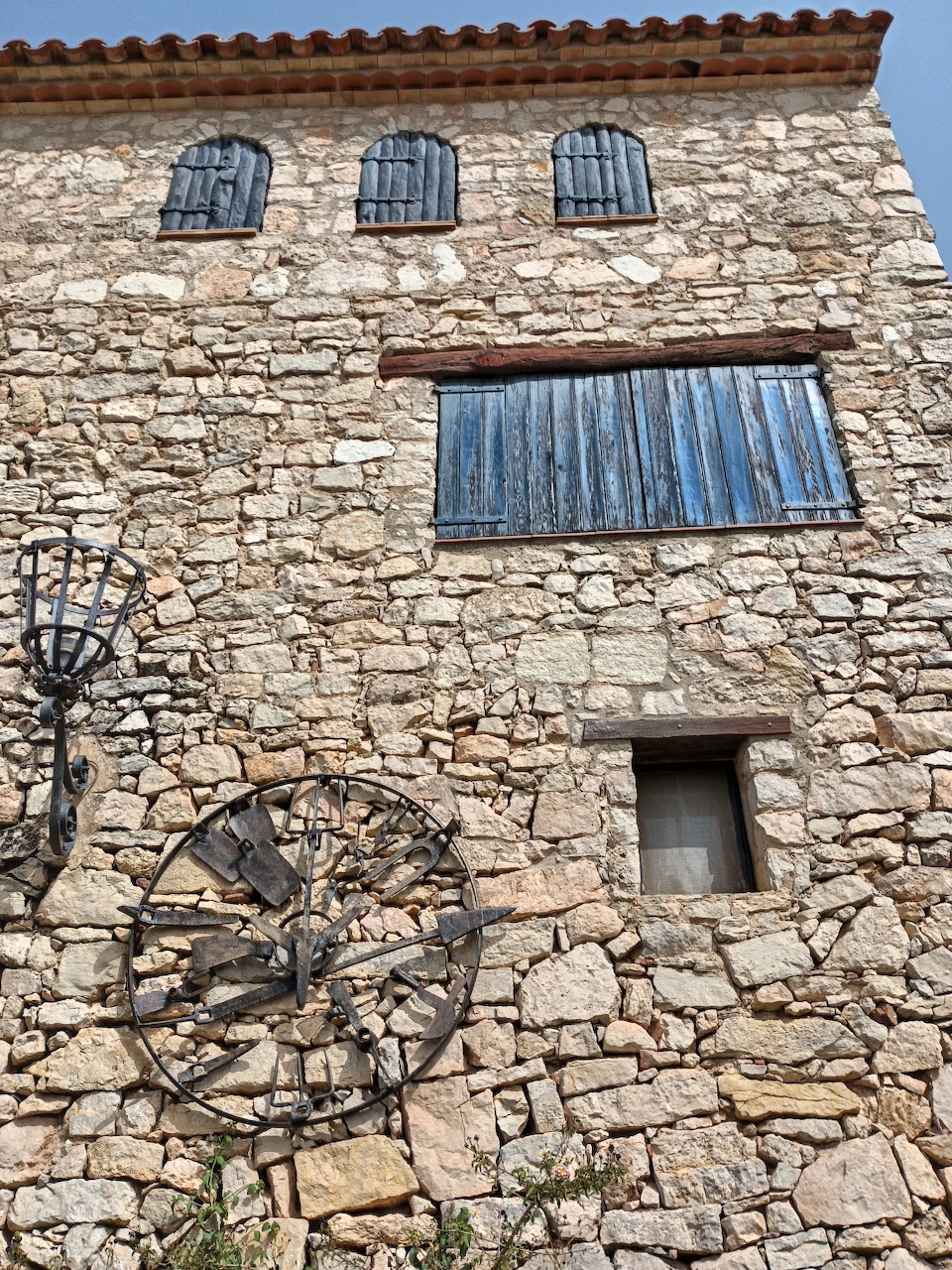 Old stone house facade with shuttered windows and a wooden wagon wheel on the wall
