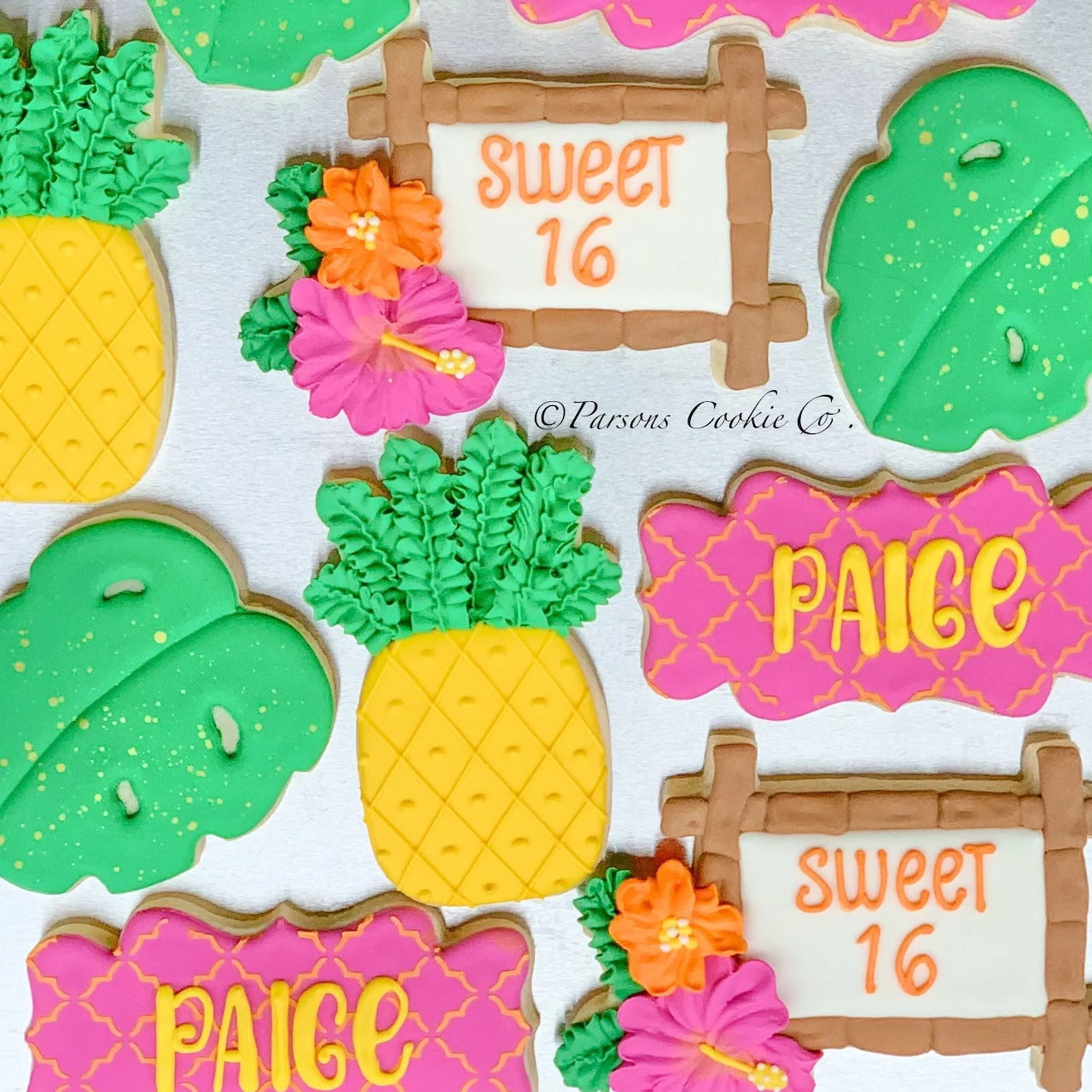 Decorated tropical themed sugar cookies with pineapples, monstera leaves, flowers, and Sweet 16 signs