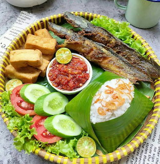 Grilled catfish with rice, sambal, cucumber, tomato, tofu and tempeh on banana leaf