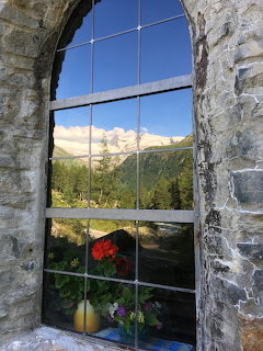 Stone chapel window framing reflection of snowy mountain peak and alpine valley