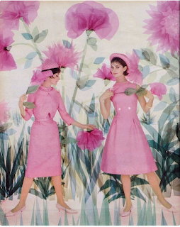 Two women in pink1960s dresses and hats posing against a pink floral and green foliage backdrop