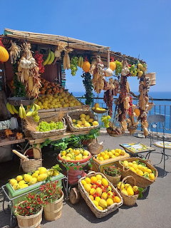 Outdoor fruit stand with baskets of lemons, oranges, and vegetables on the Amalfi Coast with sea view