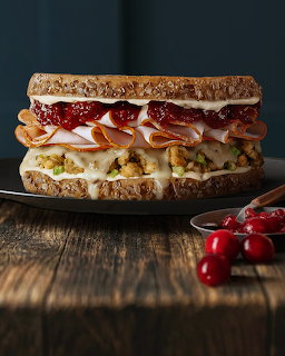 Stacked turkey sandwich with cranberry sauce, stuffing, and melted cheese on whole grain bread on a dark plate