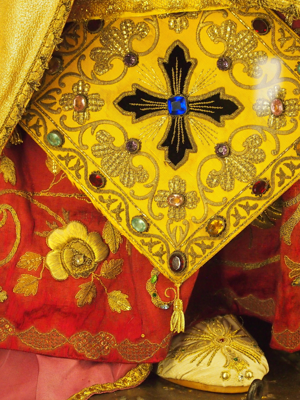 Close-up of red and gold embroidered fabric with floral motifs and a jeweled yellow panel
