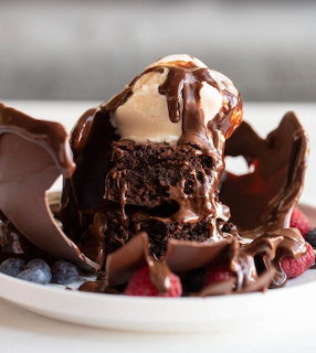 Chocolate brownie with melting vanilla ice cream, chocolate sauce, berries and chocolate pieces on white plate