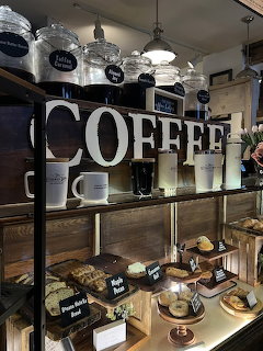 Coffee shop shelving unit with COFFEE sign, glass jars, mugs, and pastry display case below