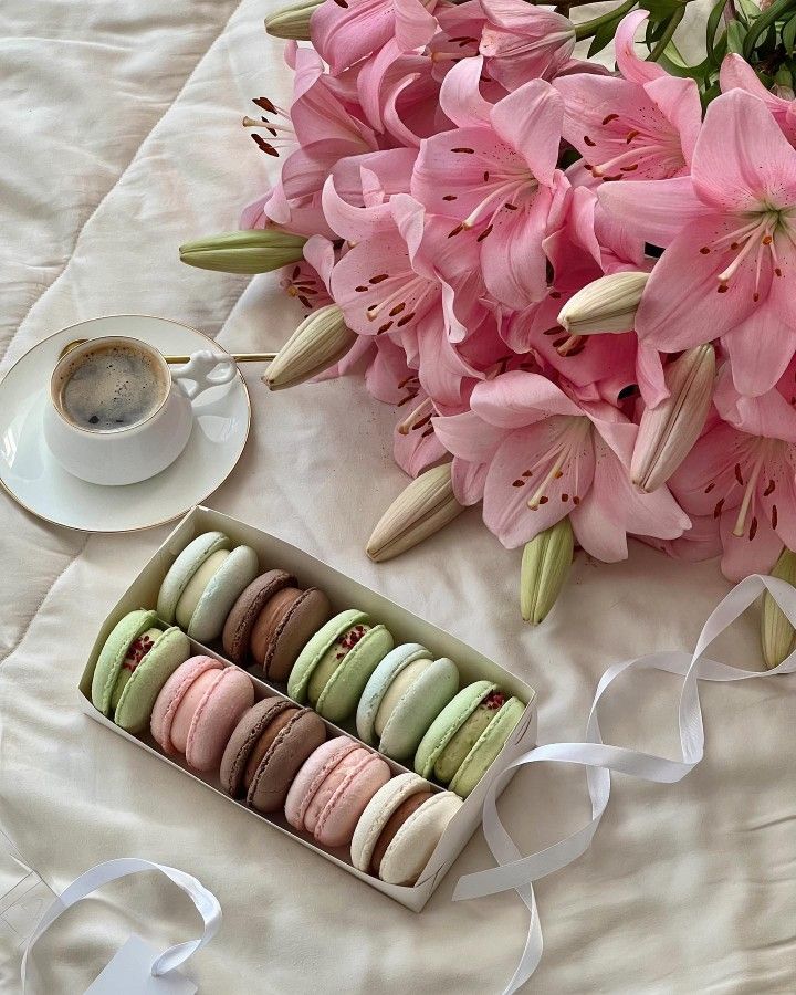 Pink and green macarons displayed with pink lily flowers and coffee on white fabric
