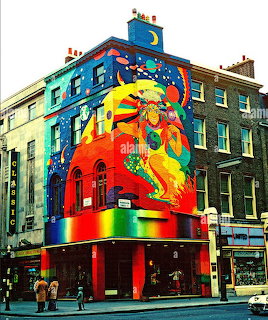 Colorful large-scale street art mural on a corner building facade with a vibrant figure and abstract designs