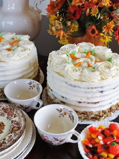 Three white frosted layer cakes decorated with fall elements, autumn flowers, and seasonal desserts on display