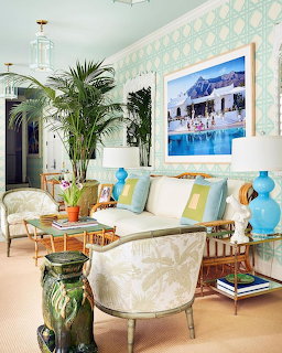 Bright tropical living room with palm plants, wicker chairs, pastel cushions, and a framed beach painting