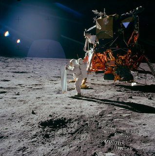 Astronaut on moon surface beside lunar module with Earth in background