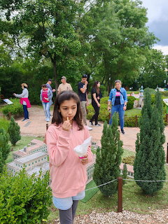 Young girl in pink hoodie eating ice cream at a miniature park with small buildings and green trees