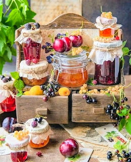 Wooden crates displaying glass jars of homemade jellies and preserves surrounded by fresh fruits and berries
