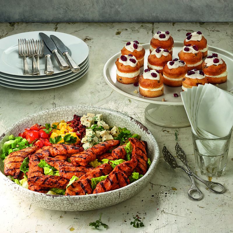 Bowl of rice with grilled chicken and vegetables next to mini fruit tarts on a kitchen counter
