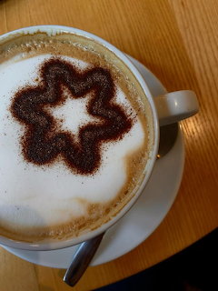 Cappuccino with decorative star pattern in cocoa powder on milk foam, white cup and saucer on wood table