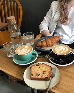 Two lattes with latte art, croissant, and cake slice on a wooden cafe table