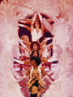 Sabrina Carpenter performing on stage with dancers and white feather decorations in pink lighting