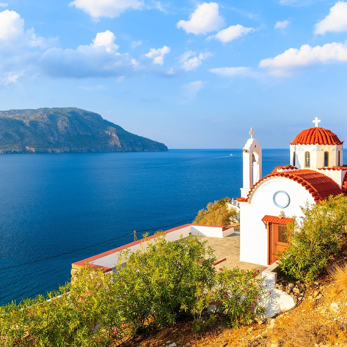 White chapel with red domes above a blue sea and distant rocky coast