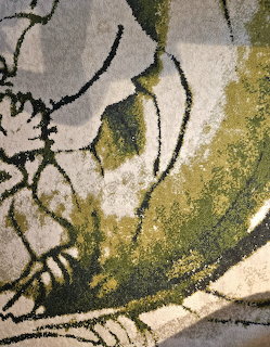 Close-up of an abstract floral pattern on a textured rug in green, gray, and cream colors