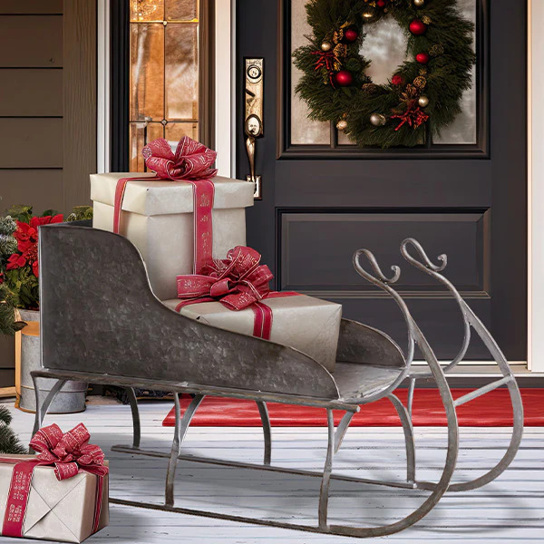Rustic sleigh with wrapped Christmas gifts on a porch beside a front door with a holiday wreath