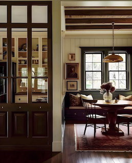 Cozy dining nook with round wood table, dark banquette, pendant light, and glass-front cabinet
