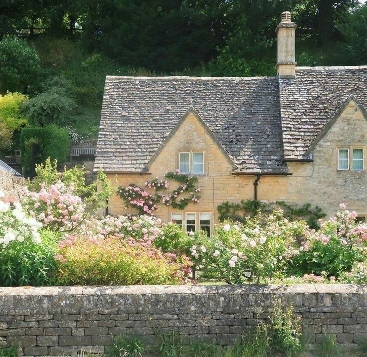 Stone cottage with climbing roses and colorful garden flowers behind a stone wall