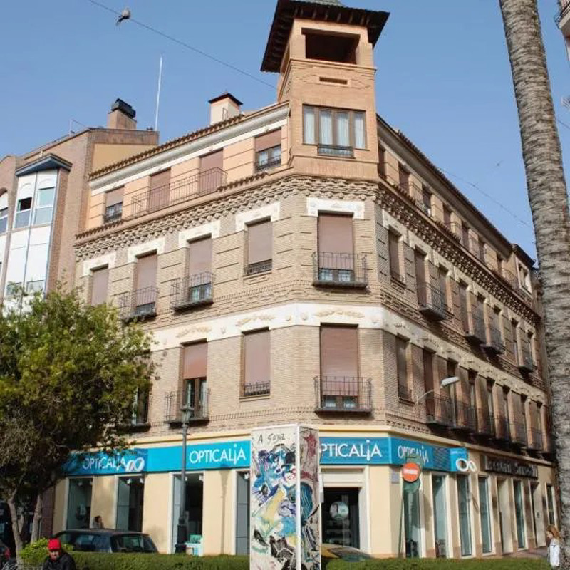 Multi-story corner building with balconies and ground-floor shops on a city street