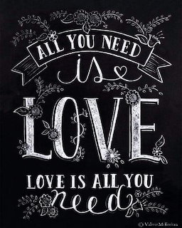Chalkboard letering art saying All You Need Is Love with floral decorations on black background