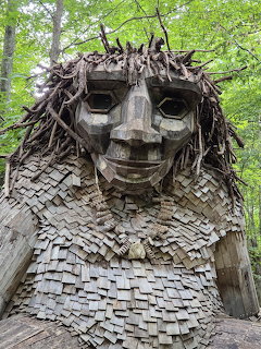 Giant smiling wooden troll sculpture with branch hair and mosaic body in forest