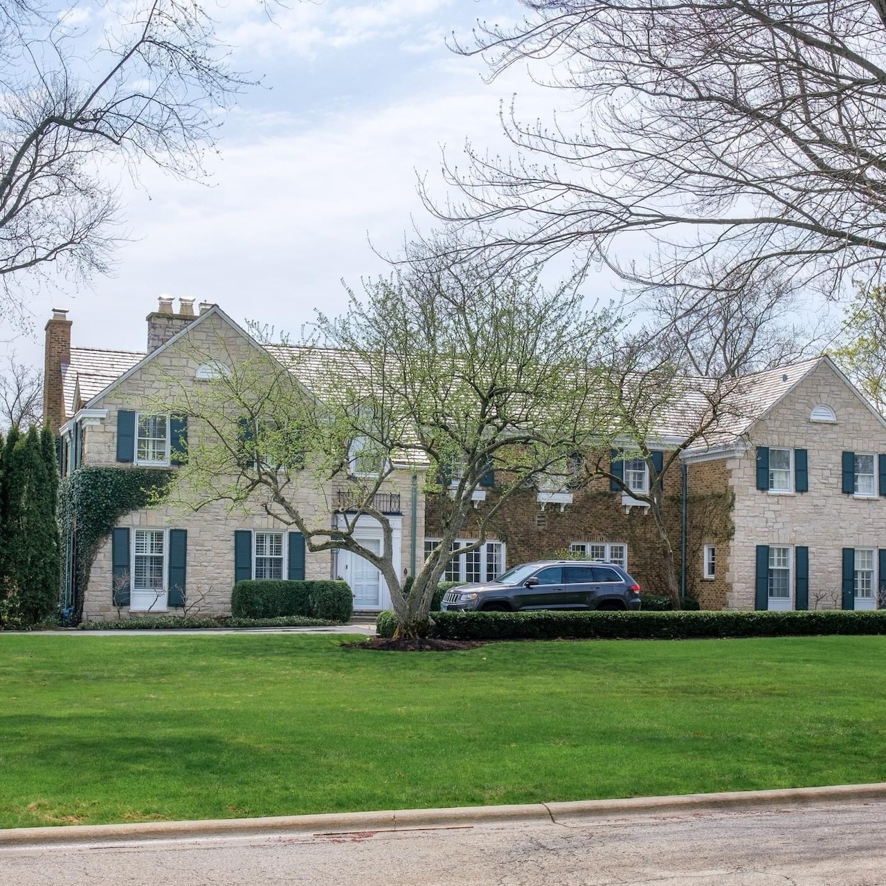 Beige two-story colonial house with green shutters and front lawn