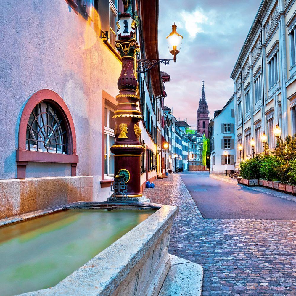 Twilight cobblestone street with colorful buildings, fountain, and distant church spire in European village