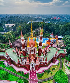 Aerial view of ornate multi-spired temple with red, white and gold towers surrounded by green landscape
