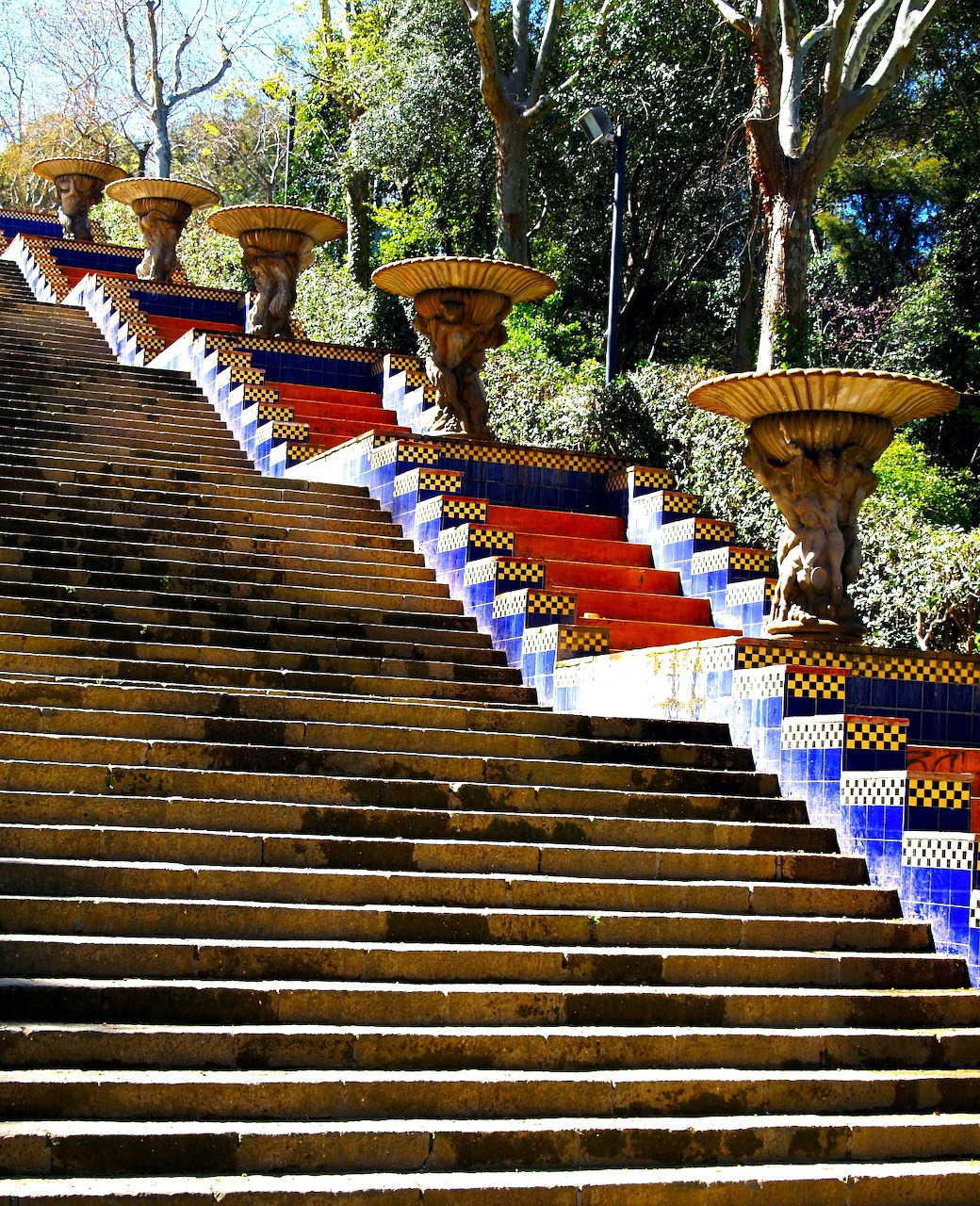 Outdoor stairs decorated with blue and yellow mosaic tiles and ornamental planters lined along the side in a park setting