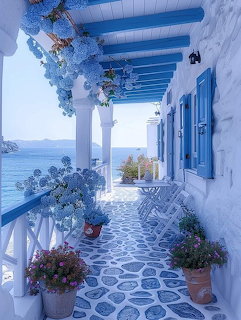 White terace with blue roof beams, columns, blue shutters, poted flowers, and ocean view in Santorini