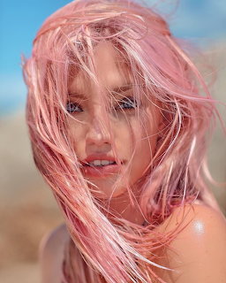 Woman with long pink hair blowing in wind, beach background
