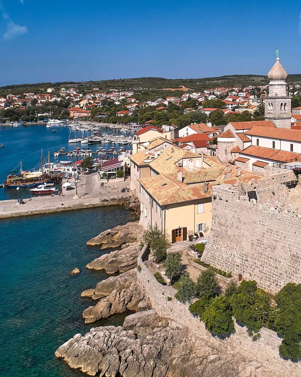 Aerial view of Krk Island town with bell tower, harbor, and turquoise sea