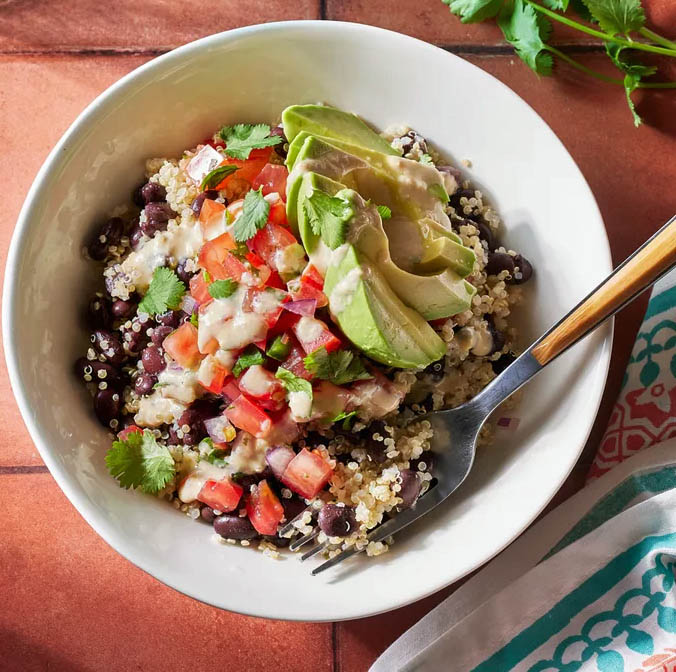 Bowl of black bean salad with quinoa, diced tomatoes, avocado, and herbs