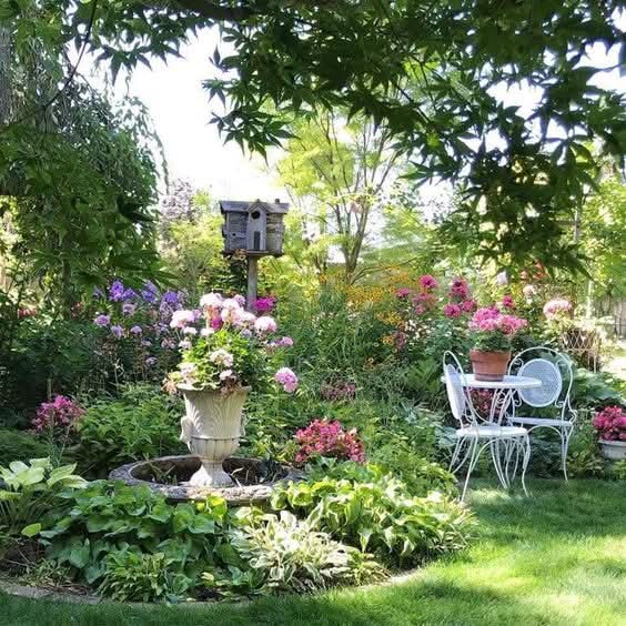 Flower-filled garden with a birdhouse and white metal patio table and chairs