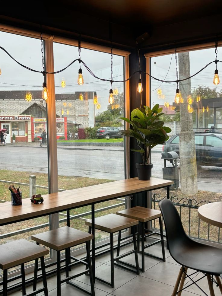 Coffee shop interior with large windows showing rainy street outside, wooden tables and hanging lights