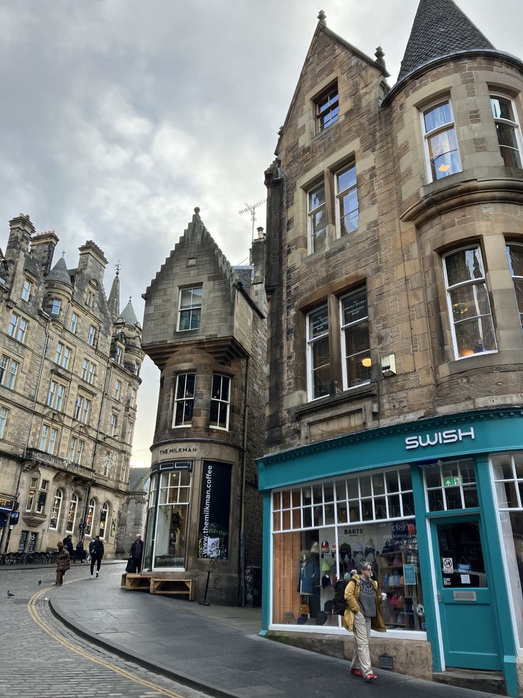 Historic stone buildings on a curved Edinburgh street with a turquoise shopfront under cloudy skies