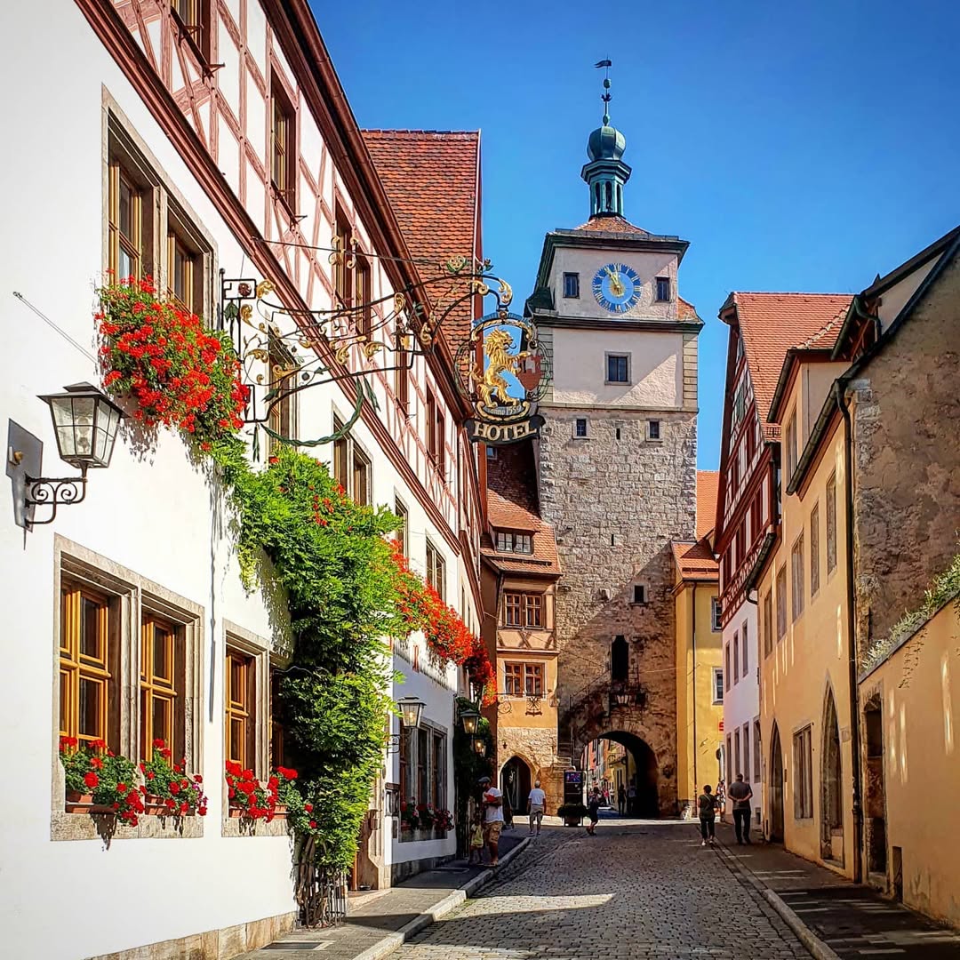 Medieval German street with half-timbered buildings, red flowers, and clock tower in Rothenburg ob der Tauber