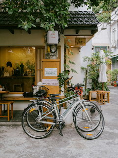 Silver bicycle parked outside a small cafe with plants and wooden furniture in a courtyard