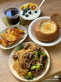 Overhead view of a meal spread with pasta, bread bowl soup, roasted potatoes, yogurt and fruit on a wooden table