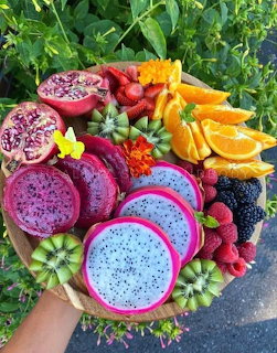 Colorful tropical fruit platter with dragon fruit, kiwi, mango, oranges, raspberries, and edible flowers