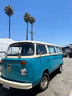 Turquoise vintage van with palm trees under blue sky in Ventura beach parking area